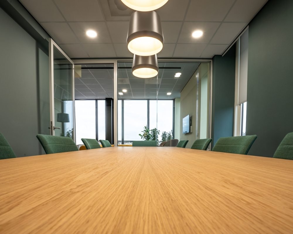 A brown table surrounded with green chairs under lamps in a room